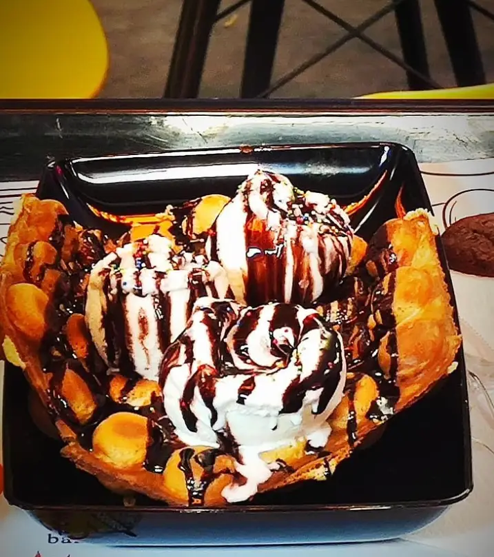 دسر لذیذ کافه لوپو: وافل حبابی طلایی با اسکوپ‌های بستنی وانیلی، سس شکلات غلیظ و ترافل‌های رنگی.