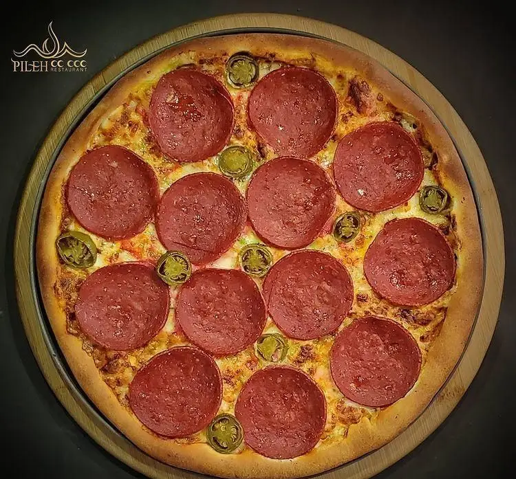 پیتزا پپرونی و هالوپینو لذیذ فست فود پیله، با پنیر فراوان و خمیر پخته شده، آماده سرو روی تخته چوبی. سفارش آنلاین پیتزا در پیله.