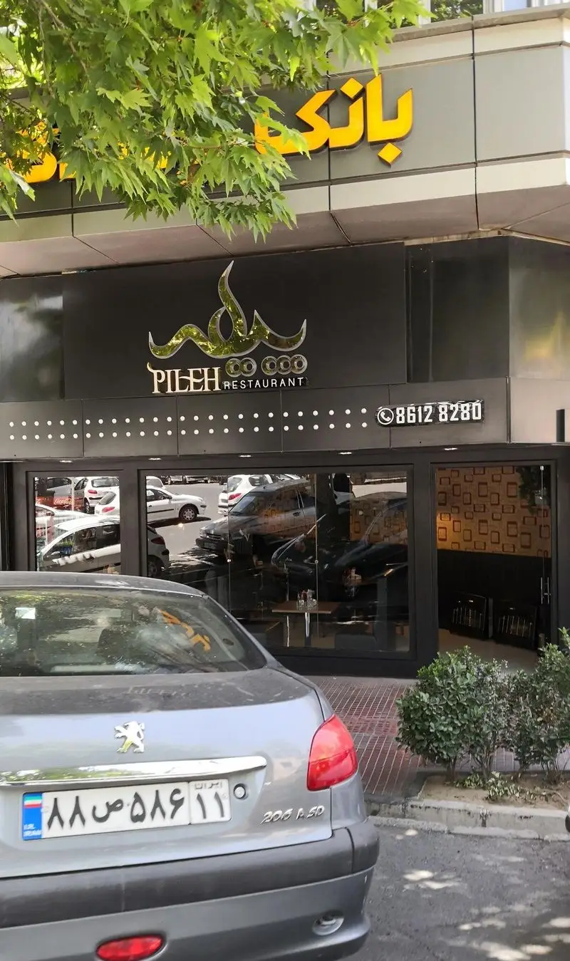 نمای بیرونی فست فود پیله با تابلوی شیک و نام تجاری برجسته. ورودی شیشه‌ای با بازتاب خیابان، یک خودرو در مقابل. شماره تماس 86128280.