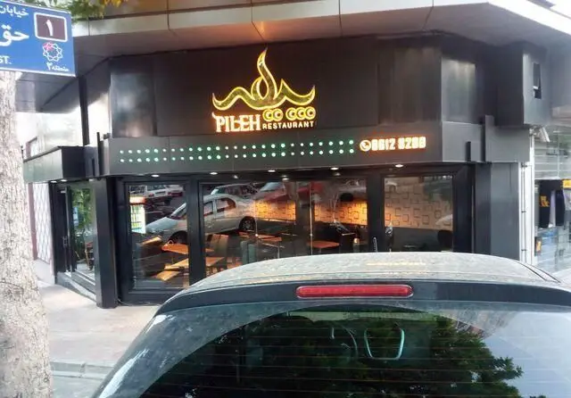 تصویری از نمای بیرونی و جذاب فست فود و رستوران پیله با تابلوی نئونی روشن، شماره تلفن ۰۸۸۱۲۸۲۸۸ و آدرس خیابان حق در روز روشن.