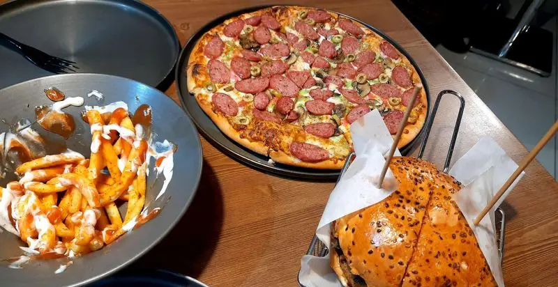 تصویری جذاب از پیتزا سوسیس، قارچ و زیتون فست فود پیله به همراه سیب‌زمینی سرخ‌کرده با سس و برگر بزرگ و خوش‌طعم.