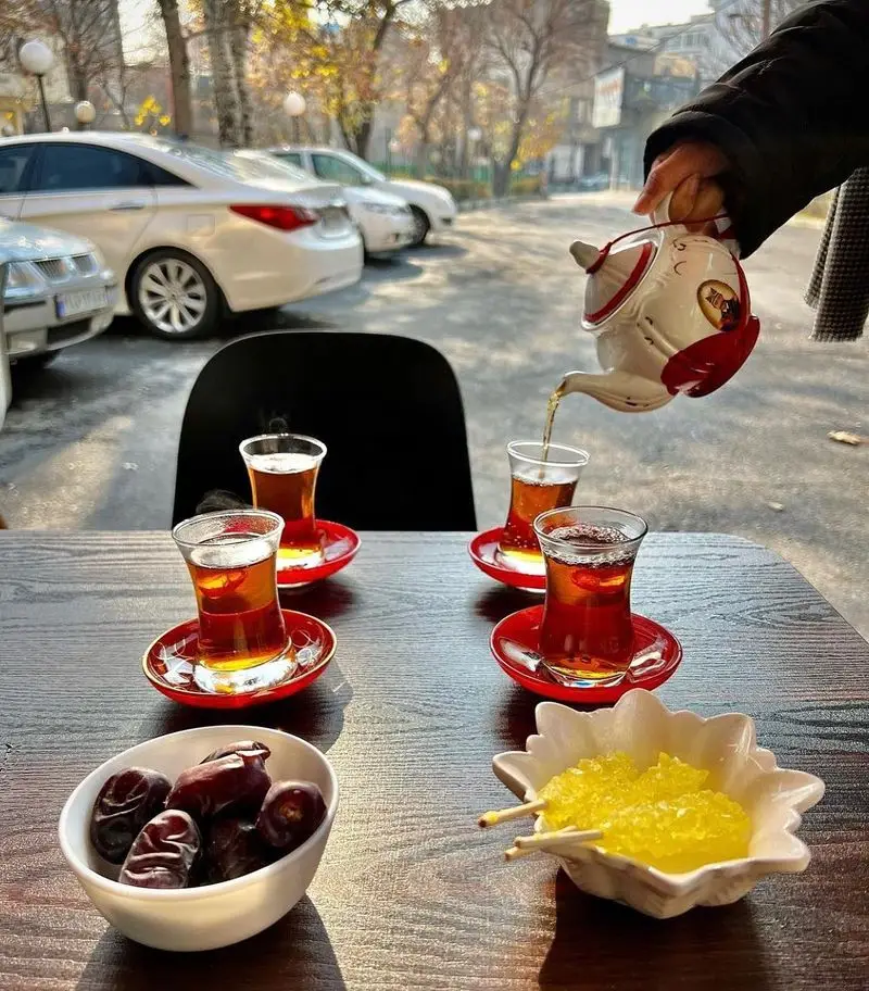 صحنه گرم و دلپذیر سرو چای ایرانی با نبات و خرما، نشان از مهمان‌نوازی کباب و جگر سرای عمو هوشنگ برای مشتریان.