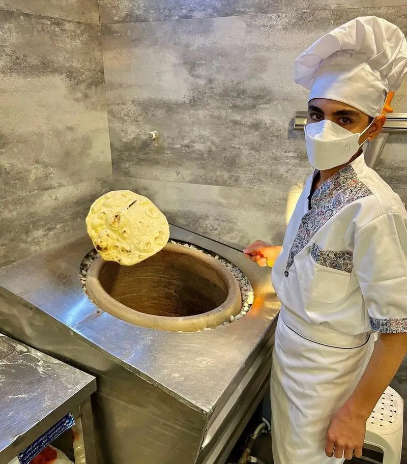 آشپز جوان و ماهر کباب و جگر سرای عمو هوشنگ در حال پخت نان داغ و تازه تنوری. نان سنتی و لذیذ، مستقیم از تنور برای شما.