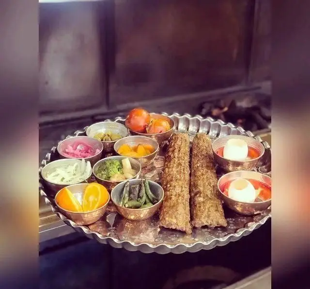 سینی کباب کوبیده عمو هوشنگ با مخلفات متنوع شامل گوجه، تخم مرغ آبپز، لوبیا سبز، پرتقال، پیاز، ترشی، زیتون و سبزیجات.