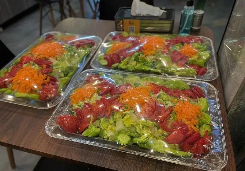 سالاد تازه و بسته‌بندی شده در کباب و جگر سرای عمو هوشنگ، شامل کاهو، گوجه، هویج و خیار، آماده برای سفارش و بیرون‌بر.