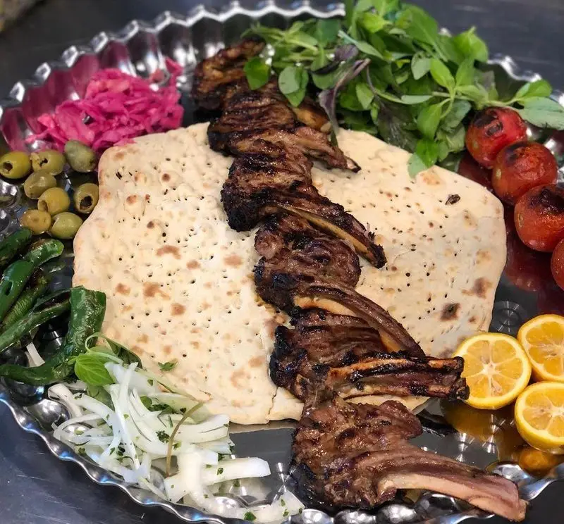 کباب شیشلیک مخصوص عمو هوشنگ با نان داغ، گوجه، زیتون، سبزیجات تازه، پیاز و لیمو در سینی مسی. طعم اصیل کباب ایرانی.