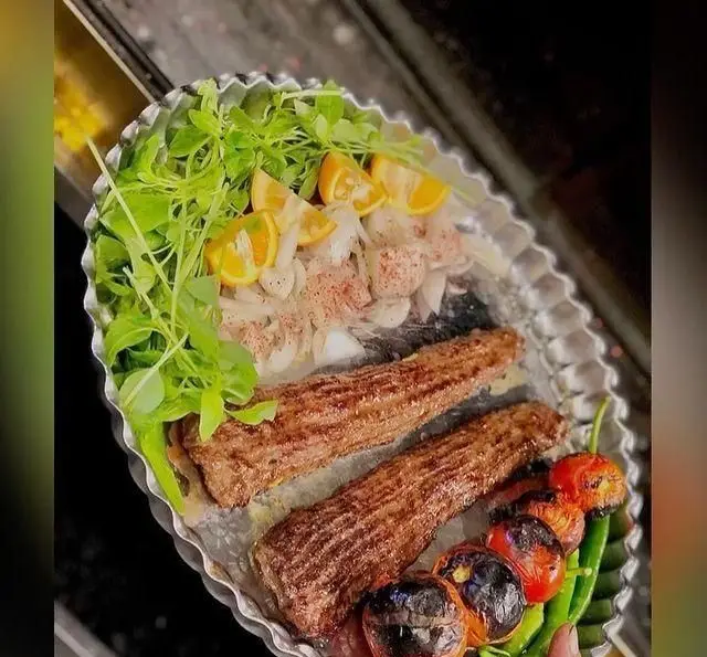 کباب کوبیده اصیل ایرانی در سینی، شامل دو سیخ با گوجه کبابی، فلفل، پیاز، سبزی تازه و نارنج، از کباب و جگر سرای عمو هوشنگ.