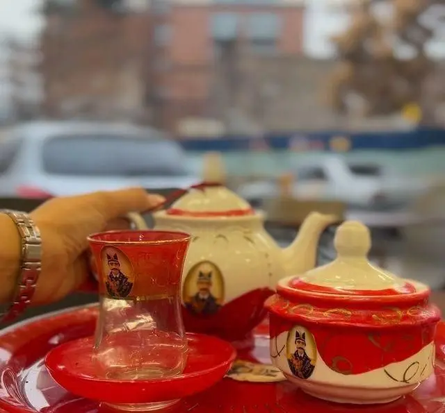 ست چای سنتی ایرانی با قوری، فنجان و قندان قرمز و سفید در کباب و جگر سرای عمو هوشنگ، نماد مهمان‌نوازی گرم.