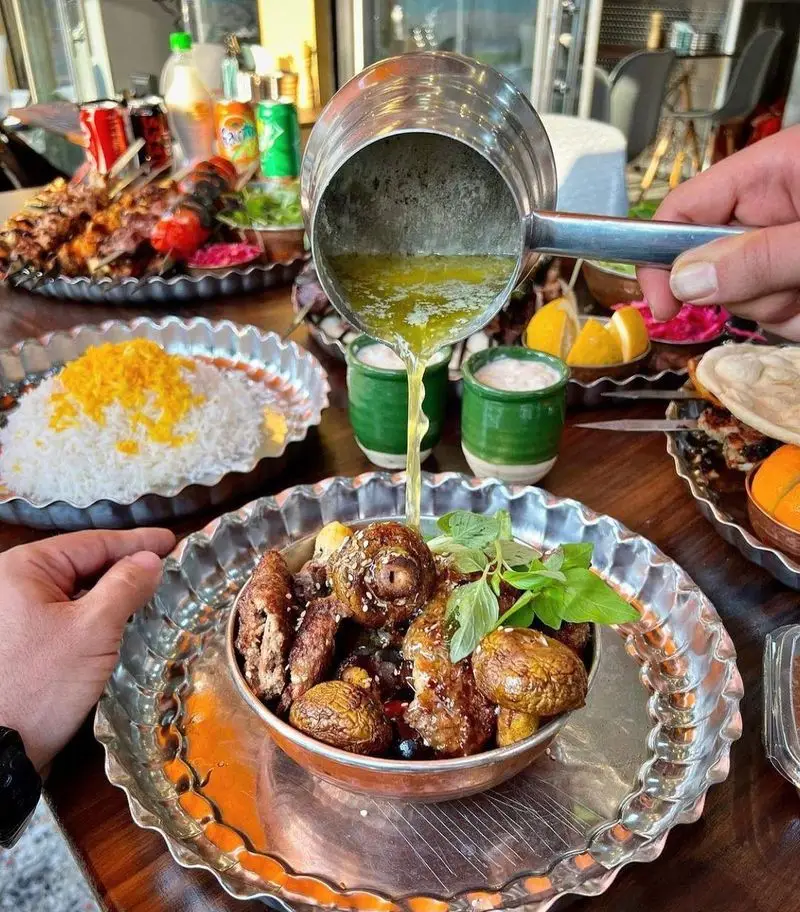 سرو غذای خوشمزه در کباب و جگر سرای عمو هوشنگ: کره ذوب شده روی بشقاب کباب و قارچ، به همراه برنج زعفرانی و مخلفات. تجربه غذای سنتی ایرانی.