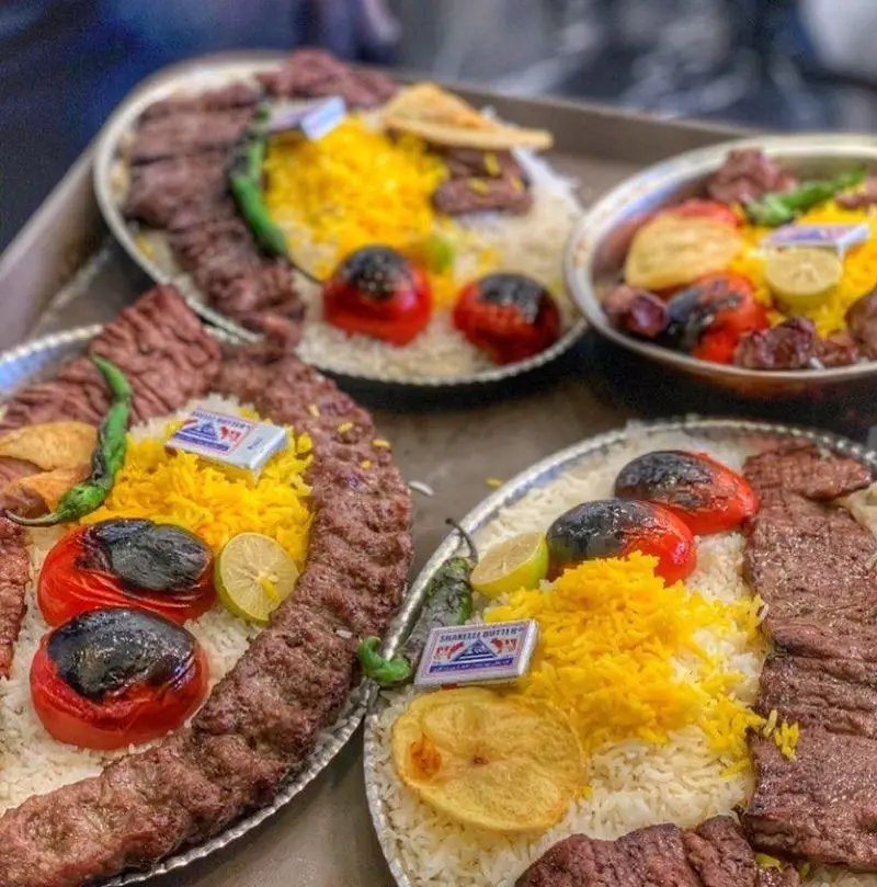 سینی‌های چلوکباب لذیذ و اصیل رستوران، شامل کباب‌های کوبیده و برگ با برنج زعفرانی و مخلفات تازه. غذای ایرانی بی‌نظیر.