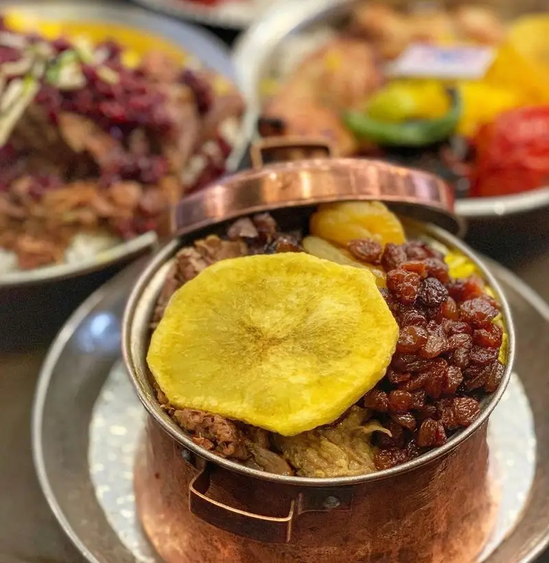 پلو ایرانی مجلسی رستوران اصیل در ظرف مسی با کشمش، میوه‌های خشک و تکه‌های گوشت. غذای سنتی و لذیذ.