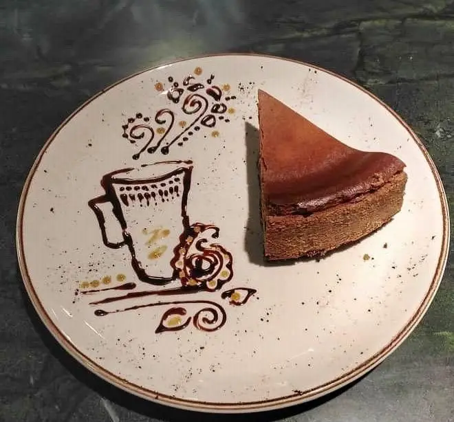 چیزکیک شکلاتی رستوران اصیل روی بشقاب سفید با تزئین هنری سس شکلات طرح فنجان قهوه. دسری جذاب و خاص.