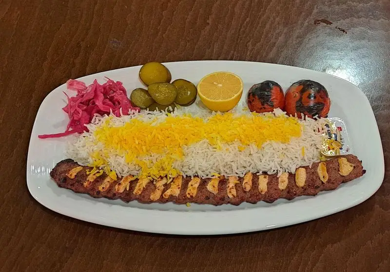 کباب کوبیده آبدار با برنج زعفرانی، گوجه کبابی، ترشی، لیمو و کره از منوی کافه رستوران آرشیو، یک غذای کامل ایرانی.