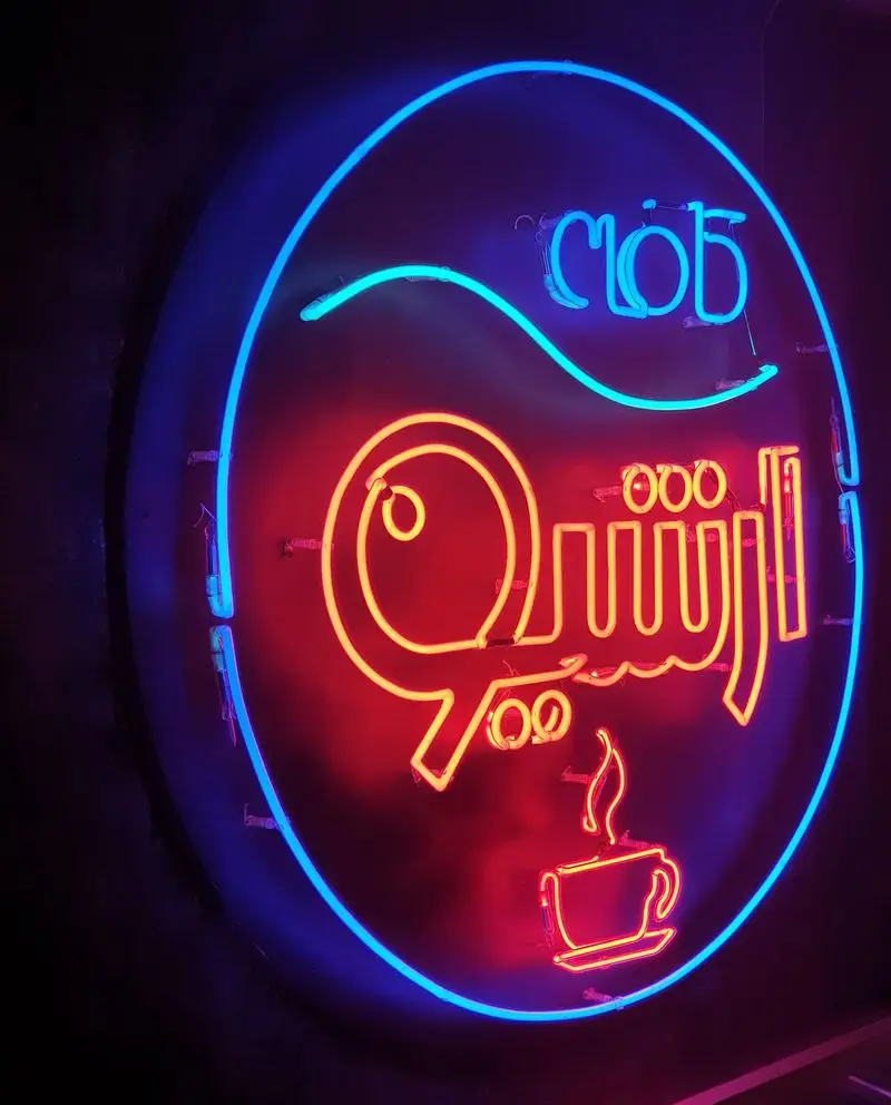 تابلو نئون جذاب و درخشان کافه رستوران آرشیو در شب. لوگوی دایره‌ای با نام "آرشیو" قرمز، فنجان قهوه و کلمه "clob" آبی.