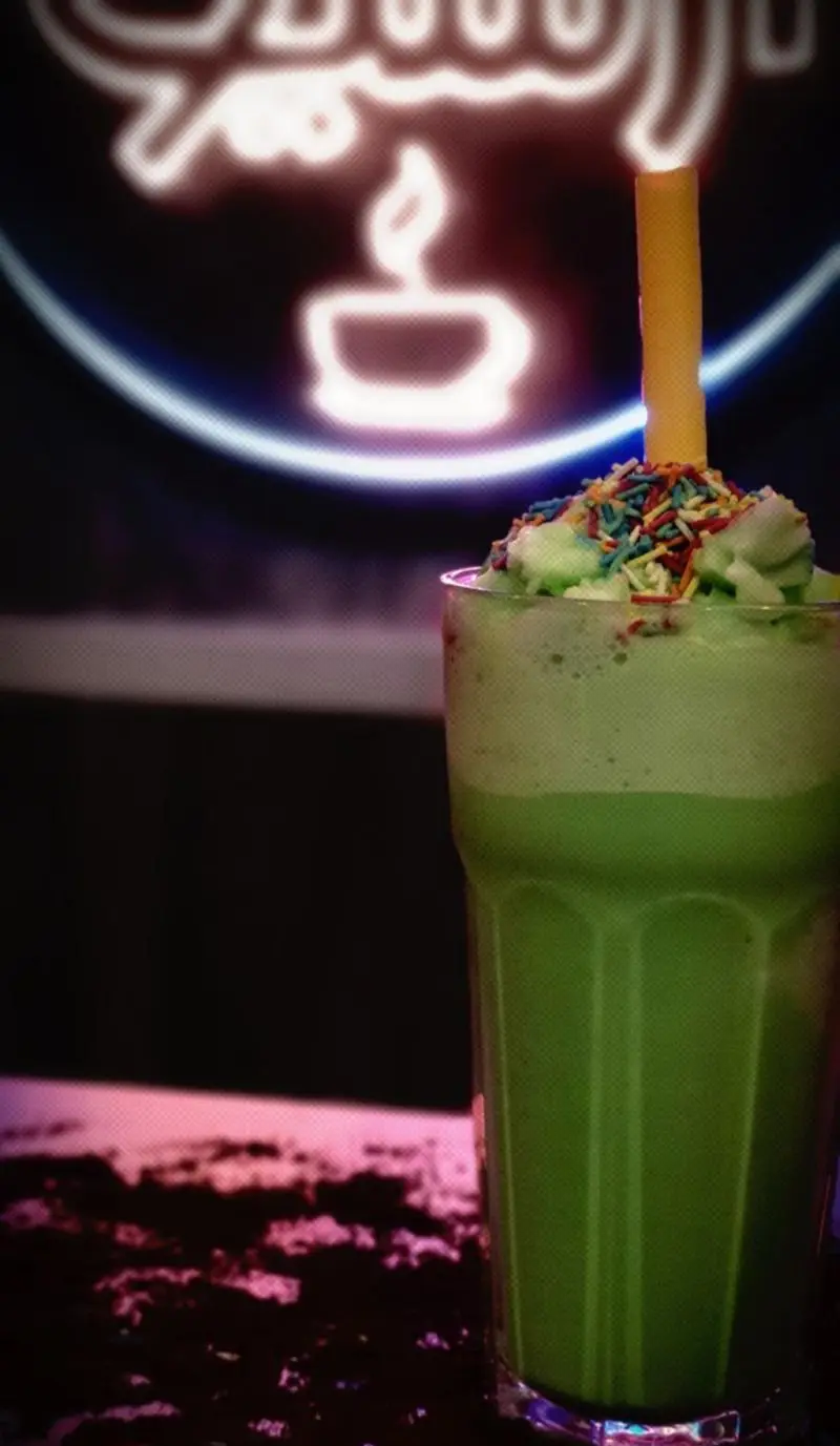 یک میلک شیک سبز رنگ خوشمزه و خنک با خامه و تزیینات رنگی جذاب در منوی کافه رستوران آرشیو برای تجربه‌ای دلپذیر.