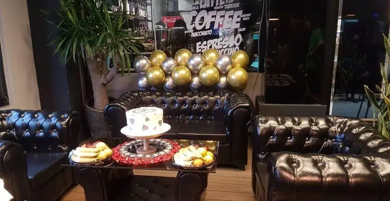 فضای داخلی فودهال نارسیس با مبلمان چرمی شیک، میز قهوه با کیک و میوه، و دکوراسیون جشن تولد و بادکنک‌های طلایی و نقره‌ای.