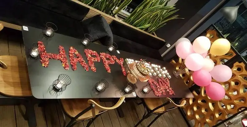 میز جشن تولد یا سالگرد شیک و رمانتیک در فودهال نارسیس، با تزیین گلبرگ های رز قرمز، کیک و بادکنک های رنگی، ایده‌آل برای ساختن لحظات خاطره‌انگیز.