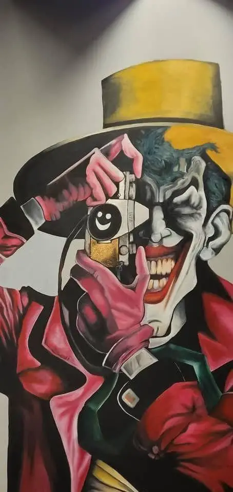 نقاشی هنری و جذاب جوکر بتمن با کلاه زرد و کت قرمز، در حال استفاده از دوربینی با نماد لبخند، اثری خاص برای فودهال نارسیس.