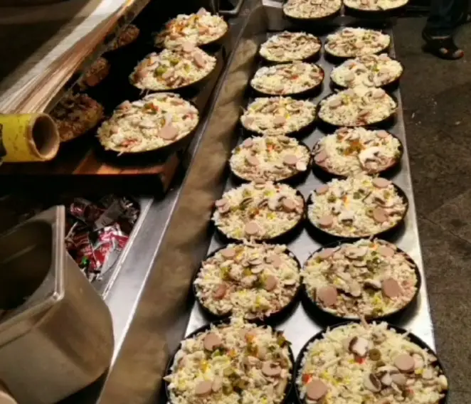 خط تولید پیتزاهای نوبهار: پیتزاهای خام با حجم بالای پنیر، سوسیس و قارچ تازه، آماده پخت و ارائه به مشتریان.