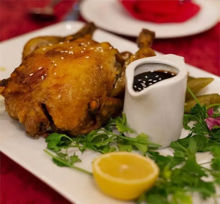 تصویری جذاب از مرغ بریان کامل و ترد با کنجد، همراه با سس مخصوص، لیمو تازه و سبزیجات معطر در رستوران دف. تجربه طعم بی‌نظیر.