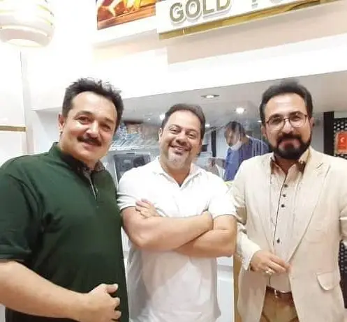 سه مرد خوشحال و خندان در محیطی دلپذیر از فست فود گلد فود، تجربه مشتری‌مداری عالی را به تصویر می‌کشند.