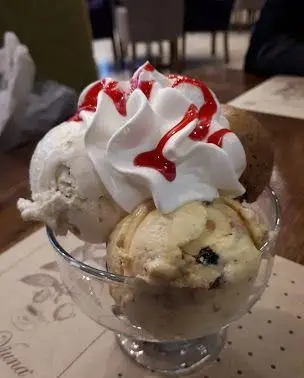 بستنی چند اسکوپ متنوع و خوش طعم شامل وانیل، کوکی و شکلات با تزئین خامه و سس قرمز در کافه ویونا. دسری خنک و لذیذ.