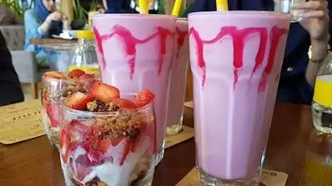 میلک شیک توت فرنگی صورتی با تزئین سس و پارفه گرانولا با توت فرنگی تازه در کافه ویونا، لذت یک عصر دلپذیر.