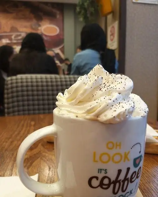 تصویر یک فنجان قهوه پر از خامه و تزئین شده با پودر در کافه ویونا، محیطی آرام برای مشتریان که از نوشیدنی لذت می‌برند.