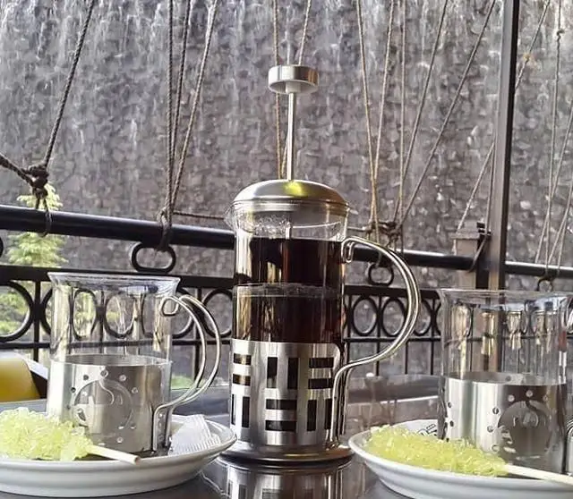 فضایی دلنشین در کافی شاپ آبشار: چای داغ در فرنچ پرس با فنجان های زیبا و نبات. لذت نوشیدن چای با منظره آبشار.