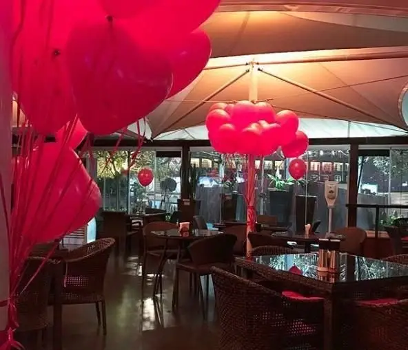 دکوراسیون رمانتیک کافی شاپ آبشار با بادکنک‌های قرمز و فضای دلنشین. میز و صندلی‌های حصیری برای تجربه عالی در مناسبت‌های خاص.