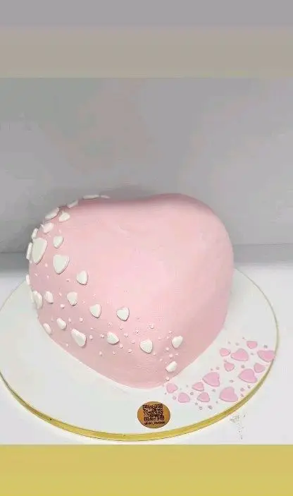 کیک قلبی صورتی رنگ شیرینی خاتون با تزئین دلنشین قلب‌های سفید برجسته و قلب‌های صورتی روی صفحه کیک، مناسب ولنتاین و سالگرد.