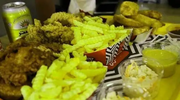 تصویری از میز فست فودهای بازيلیکو آریانو با مرغ سوخاری ترد، سیب زمینی سرخ کرده موج دار، وج سیب زمینی، سس و نوشیدنی.