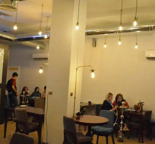 فضای داخلی دنج و مدرن کافه رستوران و قلیان بار ویوان با مشتریان در حال گفتگو و استفاده از قلیان، میز و صندلی‌های شیک و نورپردازی زیبا.