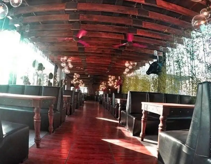 فضای داخلی شیک رستوران ایرانی ته دیگ: چیدمان میز و صندلی‌های چرمی، کفپوش چوبی قرمز، سقف دکوراتیو و نورپردازی گرم، آماده پذیرایی.