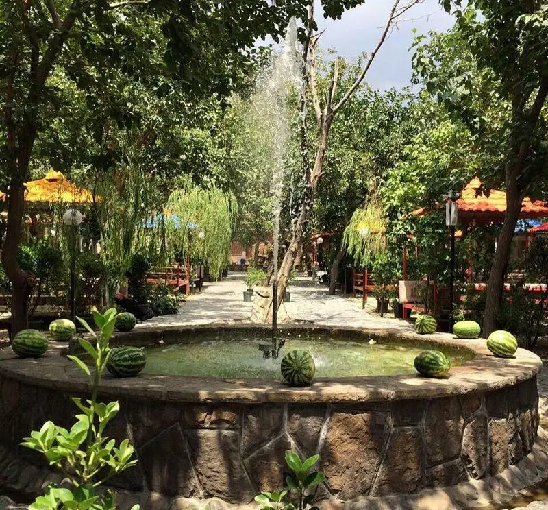 فضای زیبای باغ رستوران کاخ سنگی با حوض سنگی آبنما، درختان سرسبز و هندوانه ها، محیطی دلنشین برای مشتریان