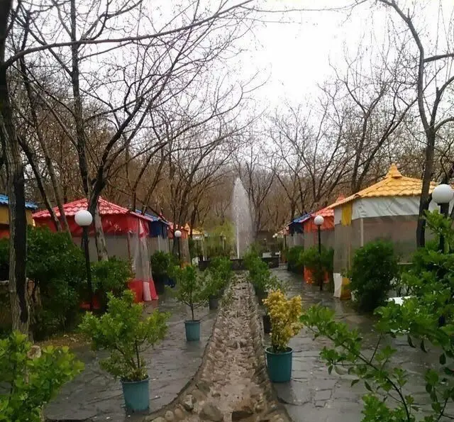 باغ دلنشین رستوران کاخ سنگی با آلاچیق‌های متنوع، فواره زیبا و مسیر سنگفرش، محیطی آرامش‌بخش برای تجربه غذایی لذت‌بخش در فضای باز.