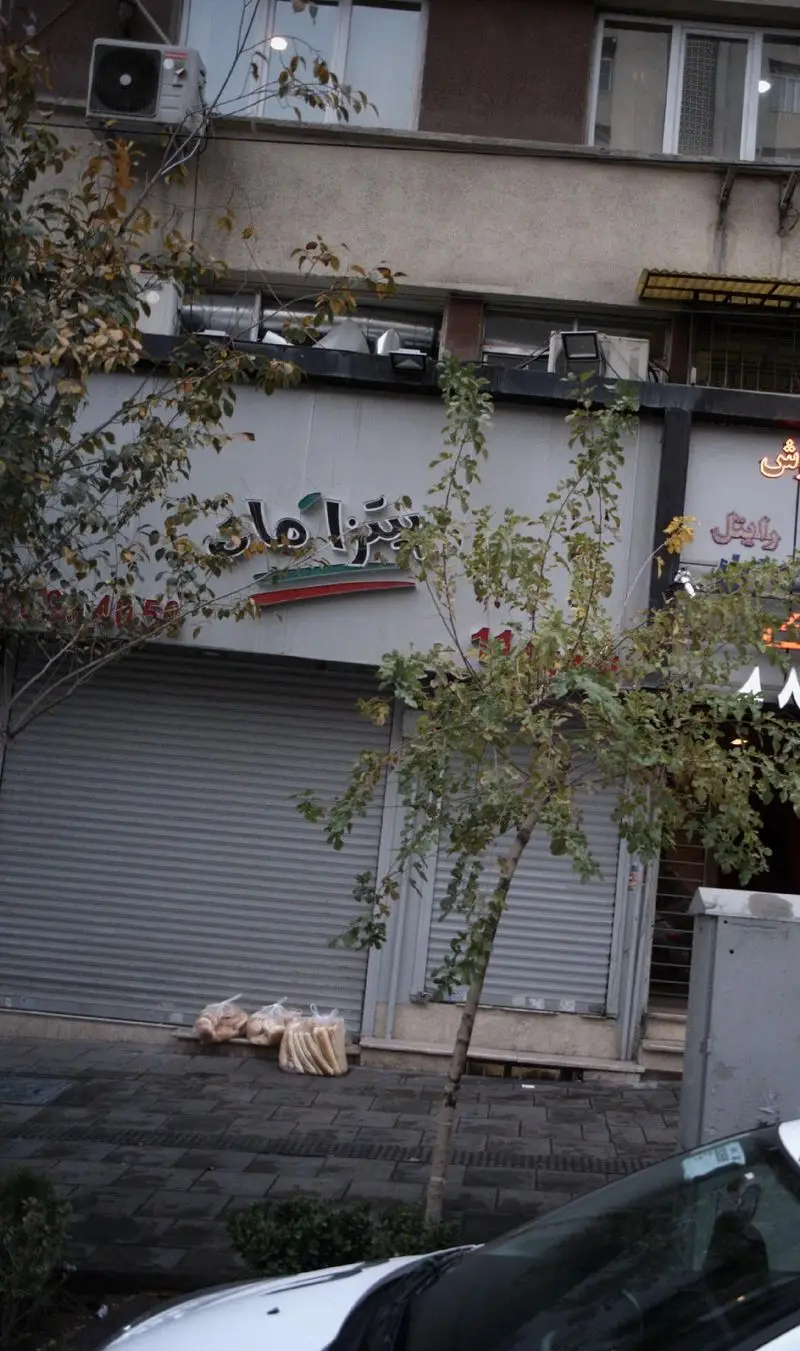 نمای بیرونی کسب و کار پیتزا هات (امیرآباد) با کرکره‌های بسته، نشان رستوران و نان‌های آماده روی پیاده‌رو تهران.