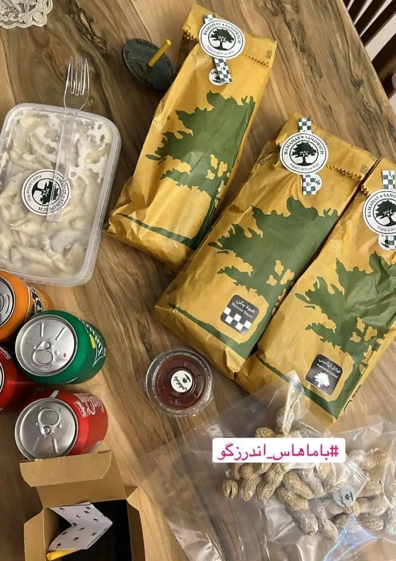 سفارش غذای باماهاس اندرزگو شامل چندین ساندویچ با بسته‌بندی خاص، سالاد، نوشابه، بادام زمینی و سس آماده برای لذت بردن از یک وعده خوشمزه.