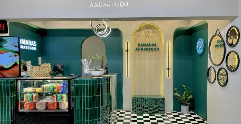 فضای داخلی مدرن باماهاس اندرزگو با دکوراسیون سبز و سفید، پیشخوان کاشی‌کاری شده، یخچال نوشیدنی و کف شطرنجی. طراحی شیک و دلپذیر برای کافه.