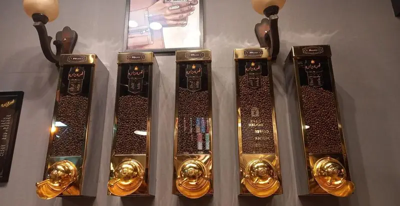 نمای داخلی کافه دانژه با پنج دیسپنسر طلایی پر از دانه قهوه تازه و مرغوب، آماده برای انتخاب مشتریان.