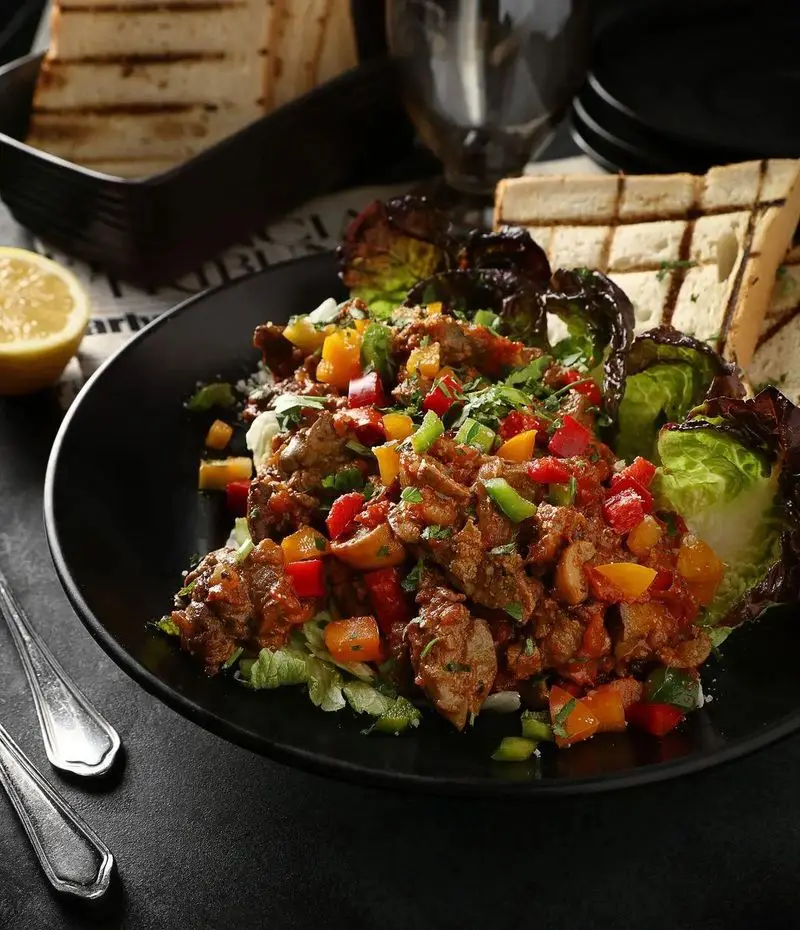 نمایی نزدیک از خوراک گوشت و فلفل دلمه رنگی سرو شده با کاهو و نان گریل در رستوران ایتالیایی آلین. تجربه‌ای خوشمزه.