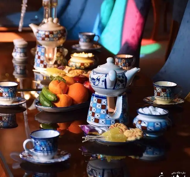 باغچه محسن: چیدمان زیبای سرویس چای خوری سنتی با قوری و فنجان‌های طرح‌دار، میوه تازه و شیرینی‌های خوشمزه.