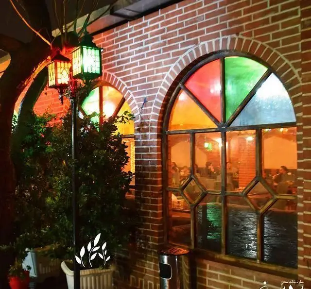 نمای بیرونی باغچه محسن، رستوران سنتی با آجرنما، پنجره‌های رنگی زیبا، نورپردازی گرم و فضای دلنشین در شب.