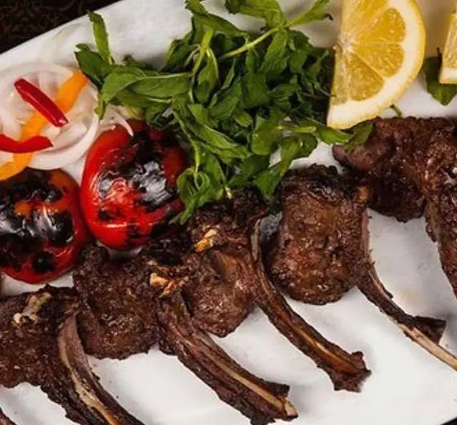 کباب شیشلیک (دنده کباب) لذیذ باغچه محسن با دورچین گوجه کبابی، فلفل، پیاز، سبزی تازه و لیمو. یک غذای مجلسی.