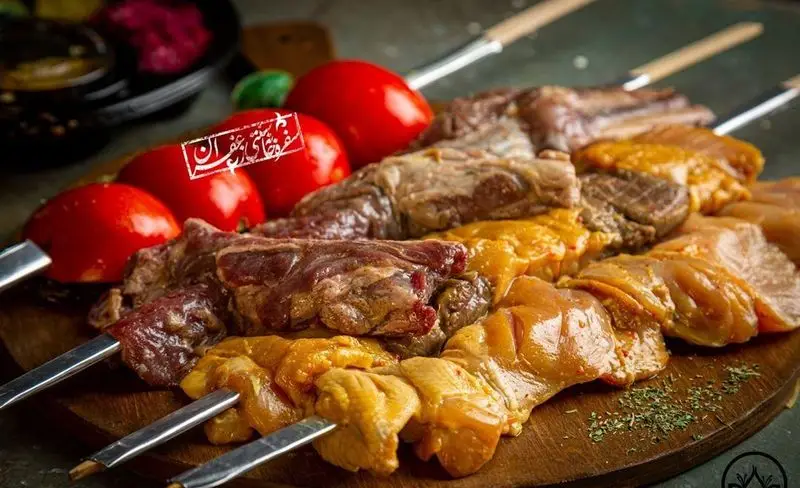 سیخ‌های کباب گوشت و جوجه مرغ تازه و گوجه‌فرنگی روی تخته چوبی، مواد اولیه باکیفیت از گل زعفرون.