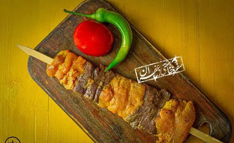 کباب چنجه و جوجه زعفرانی "گل زعفرون" با فلفل سبز و گوجه فرنگی، آماده سرو روی تخته چوبی. طعمی بی‌نظیر از غذای ایرانی.