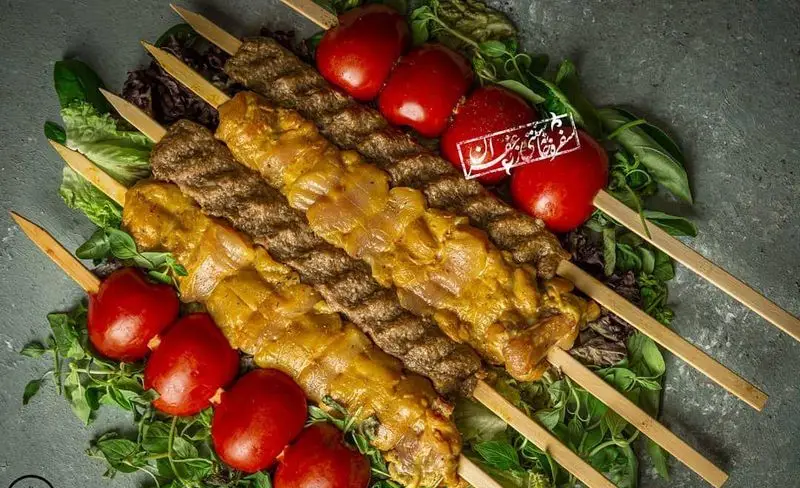 تصویر انواع کباب اصیل ایرانی شامل کوبیده و جوجه کباب زعفرانی، با گوجه کبابی و سبزی تازه. غذای لذیذ از گل زعفرون