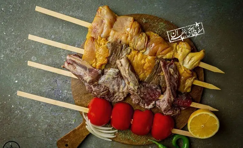 انواع کباب خام شامل جوجه، شیشلیک و گوشت تازه روی تخته چوبی، همراه گوجه، پیاز و لیمو. بهترین مواد اولیه گل زعفرون.