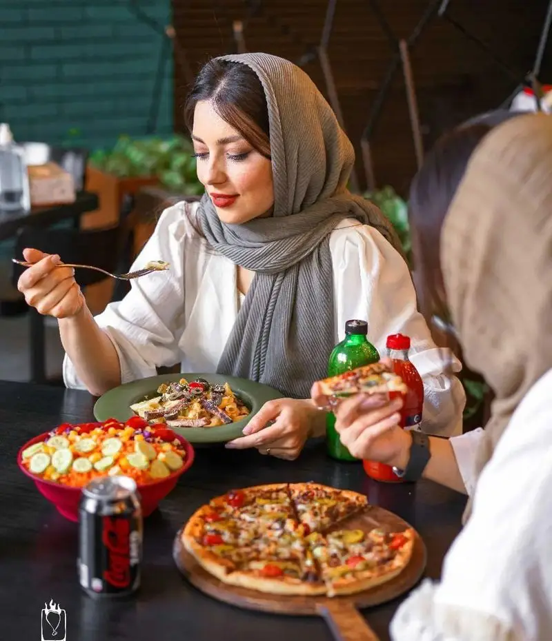 تصویری از مشتریان خوشحال در فست فود جیلیزویلیز پیروزی در حال میل کردن پیتزای تازه، پاستا و سالادهای متنوع در محیطی دلنشین.