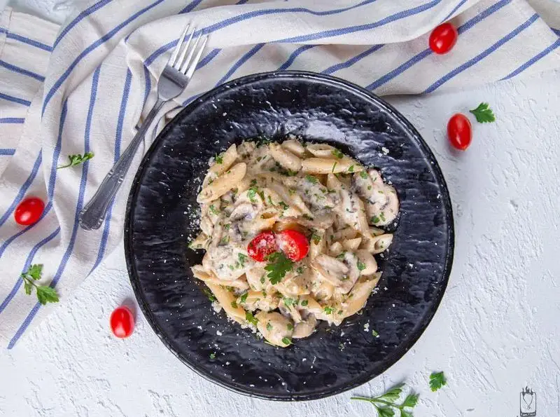 پاستا پنه کرمی با سس قارچ و خامه، تزئین شده با جعفری و گوجه فرنگی گیلاسی. غذایی محبوب و خوشمزه از فست فود جیلیزویلیز پیروزی.